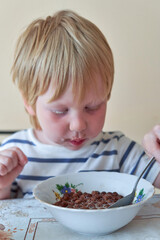 Little boy is having breakfast with chocolate balls with milk - 490997621