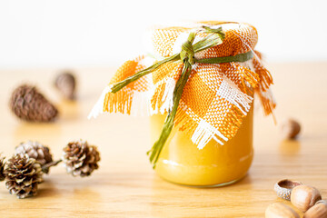 Jar of honey decorated with cloth. Organic and sweet healthy food in a glass container on a wooden table. Selective focus on the details, blurred background.