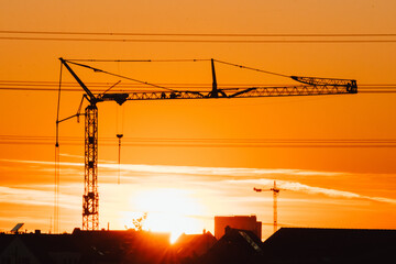 Tall construction crane silhouette in orange sky sunset shows construction site with engineering...