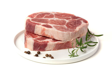 Pieces of marbled steak of raw pork or beef with a sprig of rosemary and pepper peas on a white plate on a white background.