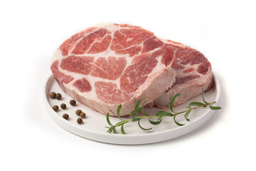Pieces of marbled steak of raw pork or beef with a sprig of rosemary and pepper peas on a white plate on a white background.