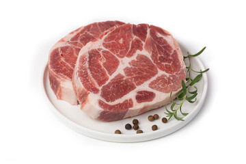 Pieces of marbled steak of raw pork or beef with a sprig of rosemary and pepper peas on a white plate on a white background.