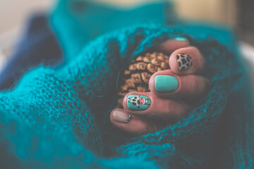 Playful colorful manicure closeup. Bright green gel polish, funny painted cow and animal pattern on fingernails. Selective focus on the details, blurred background.