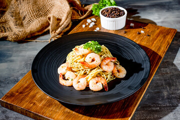italian food Prawn Aglio Olio pasta noodle with black pepper in a dish on wooden board side view on dark background