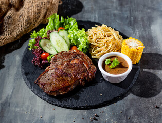 Ribeye Steak with chili sauce, salad, noodles, corn in a dish top view on dark background