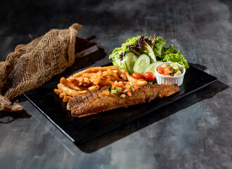 Grilled Atlantic Halibut with french fries and salad in a dish side view on dark background