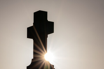Glowing cross silhouette with sunbeams sunset sunlight and clear evening sky shows christianity spirituality of church and forgiveness at grave and death for catholic resurrection metaphors on easter