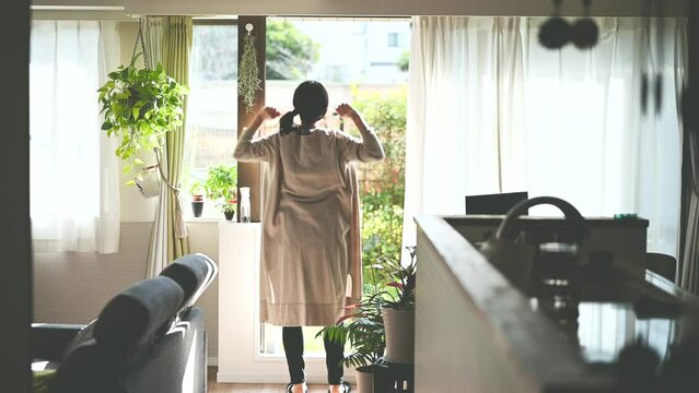 朝、カーテンを開けて伸びをする女性