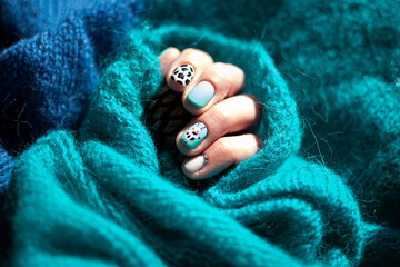 Bright sunlit manicure closeup. Cow skin pattern, painted funny animal, bright minty and blue concept. Selective focus on the details, blurred background.