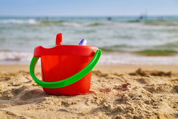 Red children's bucket in the sand on the seashore