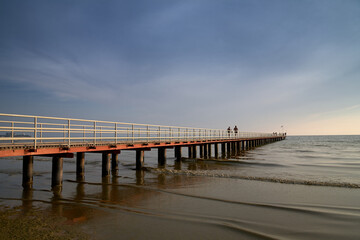 Fototapeta premium Beachfront view with people walking along the pier at sunset
