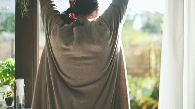 朝、カーテンを開けて伸びをする女性