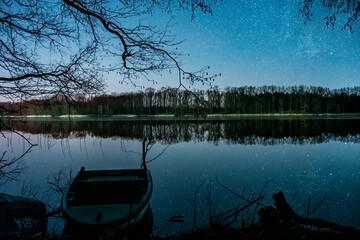 Łódka nad jeziorem w trakcie pogodnej nocy.  Łódź lub statek i gwiazdy. Łowienie ryb nocą. © MatB