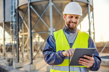 An industry worker using tablet for checking on supply in silos.