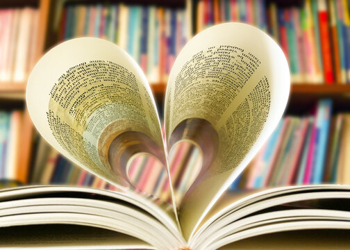 The book rests on a heart-shaped table with a library bookshelf background. Heart book page image blur.