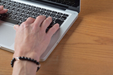 手首にパワーストーンをつけて自宅の木の机でノートパソコンで仕事をしている