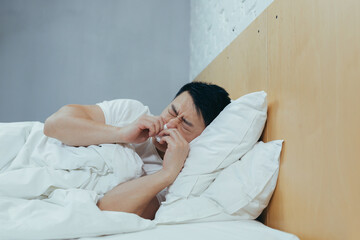 Sick man lying in bed has a runny nose cold and flu, Asian at home covered with a blanket