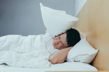 A man at home tries to fall asleep, noisy neighbors interfere with sleep, an Asian closes his ears...