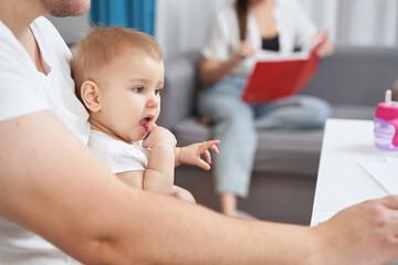 Baby on father knees putting finger in its mouth