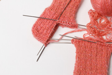 The knitting project is under implementation. A piece of knitting with a ball of yarn and knitting needles on a white background
