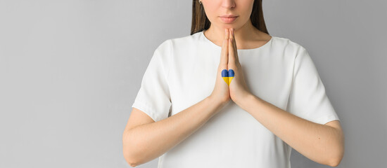 Pray for Ukraine: girl's hands with a heart of the color of the Ukrainian flag. Gray background.