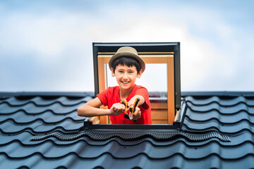Funny kid shooting wooden slingshot. The boy looks out the window on the roof of the house. Roof...