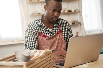Cheerful ceramist watching something on his portable computer