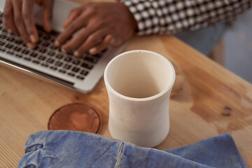 Ceramist seated at table typing on laptop