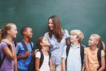 She creates such a happy classroom. A pretty young teacher standing with her classroom at the blackboard and smiling.