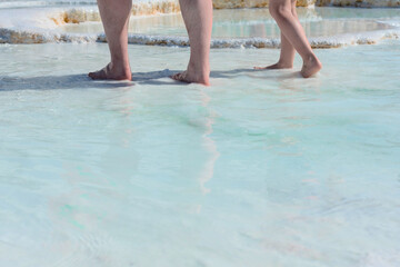Mans and childs feet standing in thermal water on white limestone terraces. Health and wellness concept. Beauty of nature