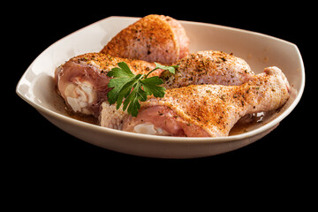 Raw chicken thighs with spices in a plate on a black background.