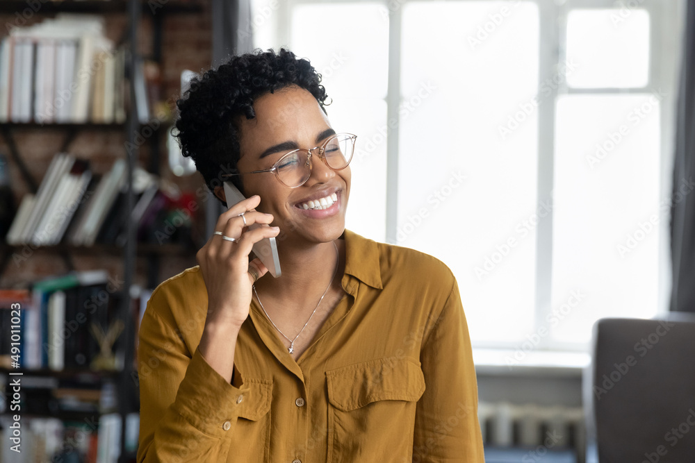 Wall mural cheerful young black entrepreneur girl in stylish glasses talking on mobile phone with happy toothy 