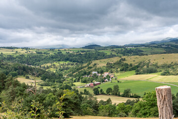 Panorama sur une vallée encaissé avec un petit village en Auvergne avec au loin l'orage qui arrive sur le superbe chemin de randonnée des pierres levées à Cournols