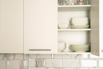 Open white kitchen cabinet door with white dishes inside