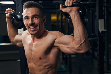 Delighted young sportsman lifting weights in the gym