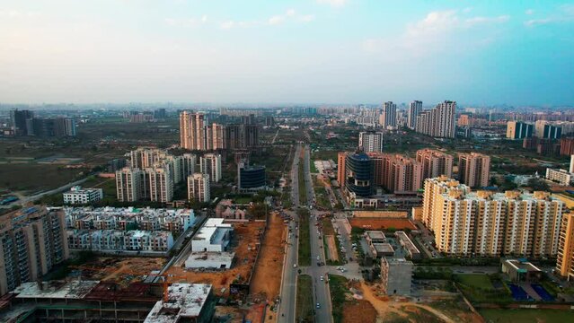 aerial shot flying over busy city street with skyscraper homes, shops and office buildings all around it on a rainy day showing developing outskirts of gurgaon, noida, delhi India