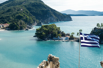 National Greek flag flying on background of beautiful seaview, Parga bay, mountains, turquoise sea in sunny weather.Travel to Greece,picturesque seascape concept.View from top, fortress