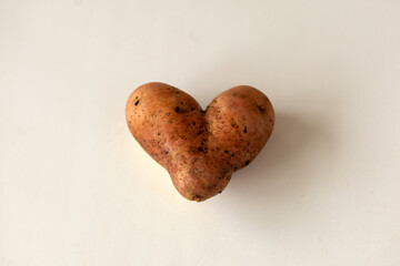 Root crop in the shape of a heart on a plain background.Funny unpeeled potato of an unusual...