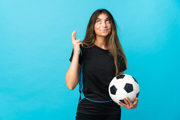 Young football player woman isolated on blue background with fingers crossing and wishing the best