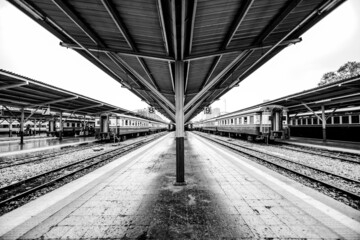 Black and white railway station platform with metal platform roof where passenger trains are parked