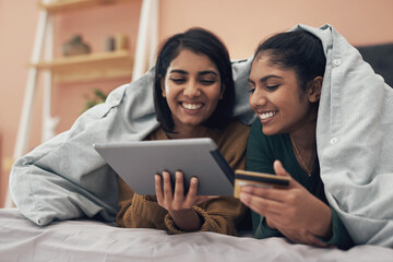 Lets just chill and have our food delivered. Shot of two young women using a digital tablet and a credit card while lying on a bed together.