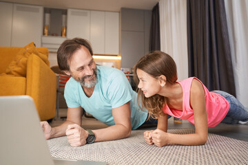 Adult man looking at teenager during plank in living room