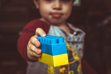Young child holding toy bricks forming Ukraine flag, Ukraine war migration crisis, stop the Russian...