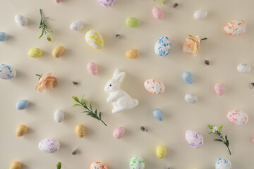 Easter and spring concept 2022. Pastel Easter concept with pastel easter eggs and spring flowers, and white Easter bunny . Easter pastel background. Creative easter arrangement.