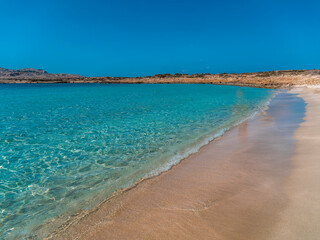 Sea waves gently touch the sandy beach under a deep blue sky