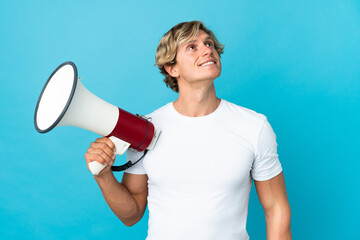 English man over isolated blue background holding a megaphone and looking up while smiling