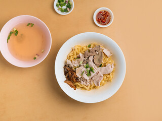 Minced meat Noodle in a bowl with soup, chili sauce and spring onion top view on wooden table