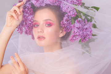 Portrait of a young girl in the studio with lilac flowers on her head, close-up. Creative beautiful make-up in doll style with lilac flowers on the head close-up.