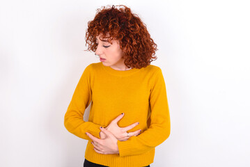 young redhead girl wearing yellow sweater over white background suffering from strong stomachache.