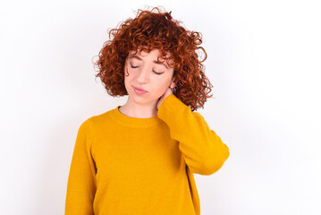 young redhead girl wearing yellow sweater over white background suffering from back and neck ache injury, touching neck with hand, muscular pain.